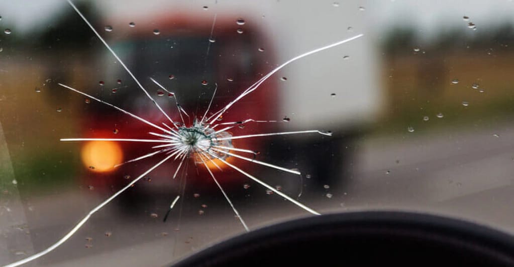 Shattered windshield caused by road debris, illustrating damage that needs replacement.